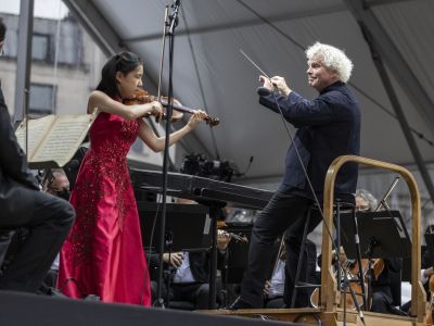 Leia Zhu wears a floor length pink dress and plays the violin, whilst being conducted by Sir Simon Rattle